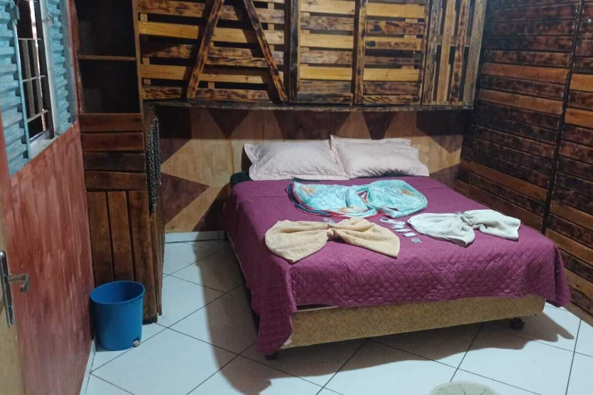 A small, cozy room with a bed, a blue bucket, and wooden walls.