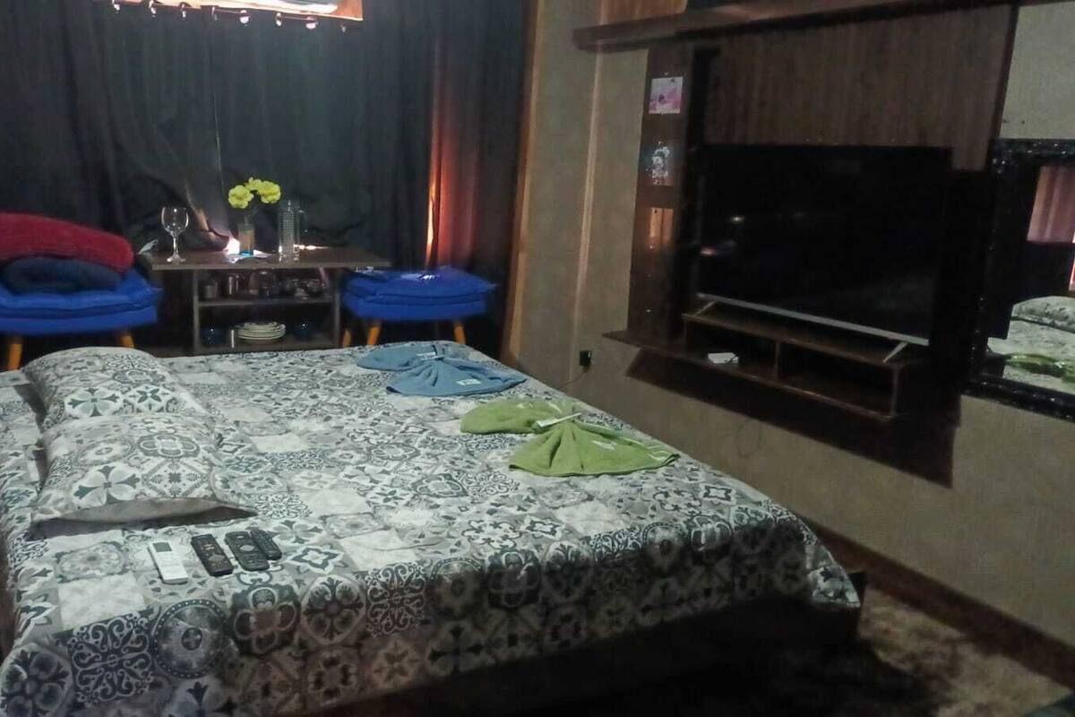 A bedroom with a patterned bedspread, a television, and a small table with a vase and a bottle.