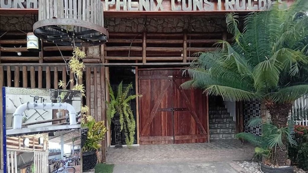 A rustic building with a wooden facade, a large wooden door, and a sign that reads "PHENIX CONSTRUCTOS". - Casarao24horas (Cuiabá)