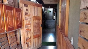 A wooden interior hallway with a tiled floor, a wooden door with decorative panels, and a staircase leading to an upper level. - Casarao24horas (Cuiabá)