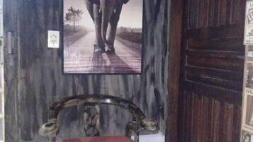 Una habitación con puerta de madera, un cuadro con un elefante en la pared y una silla de madera con cojín rojo.