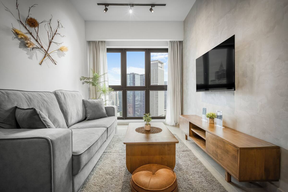 A modern living room with a grey sofa, a wooden coffee table, and a TV mounted on the wall.