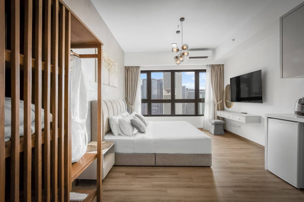 A modern bedroom with a large bed, a wooden wardrobe, a desk, and a TV.