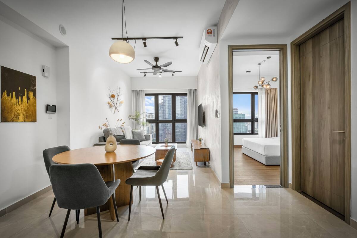 A modern living room with a dining area, a ceiling fan, and a large window offering a city view.