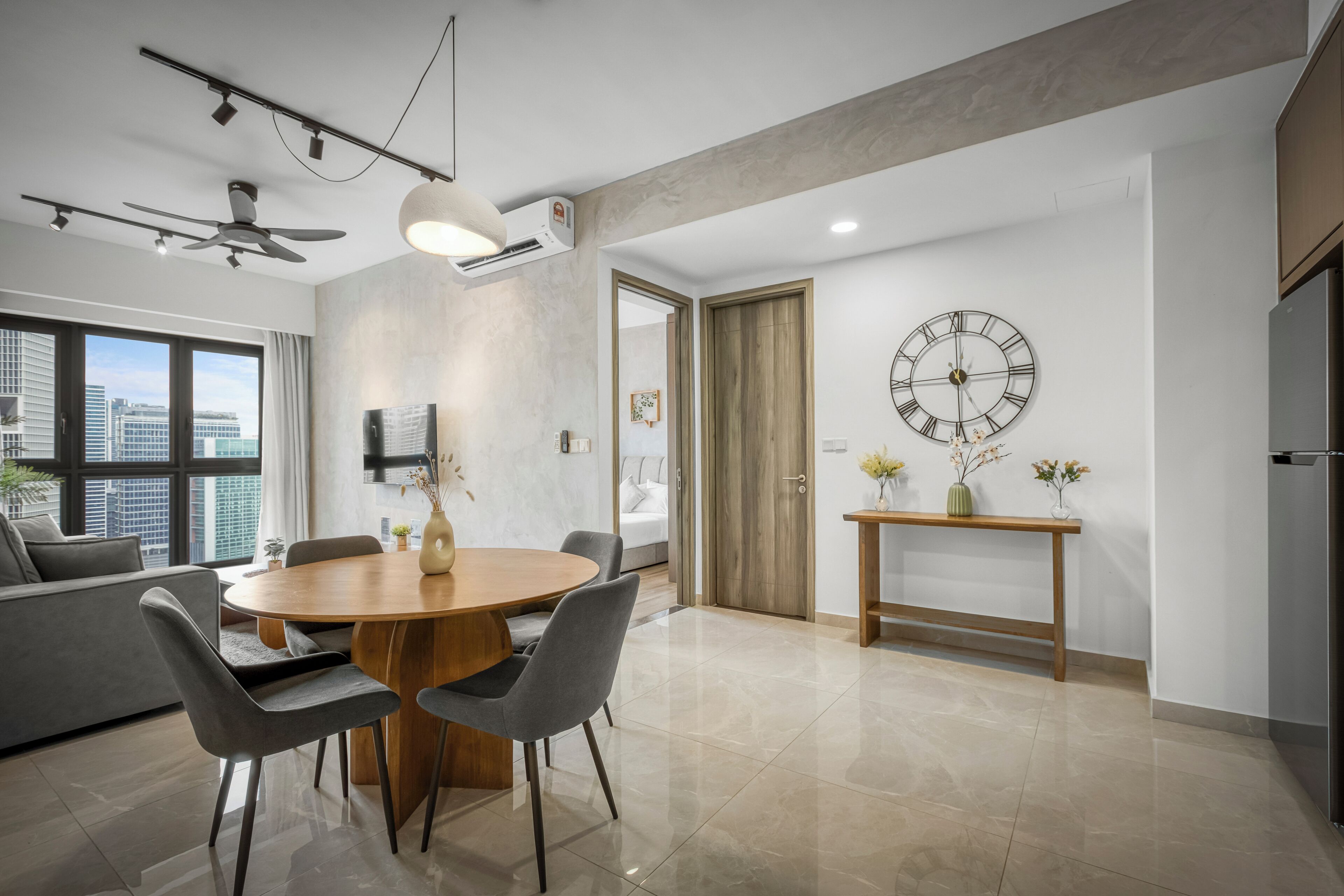 A modern dining area with a round wooden table, grey chairs, a ceiling fan, and a wall-mounted clock.