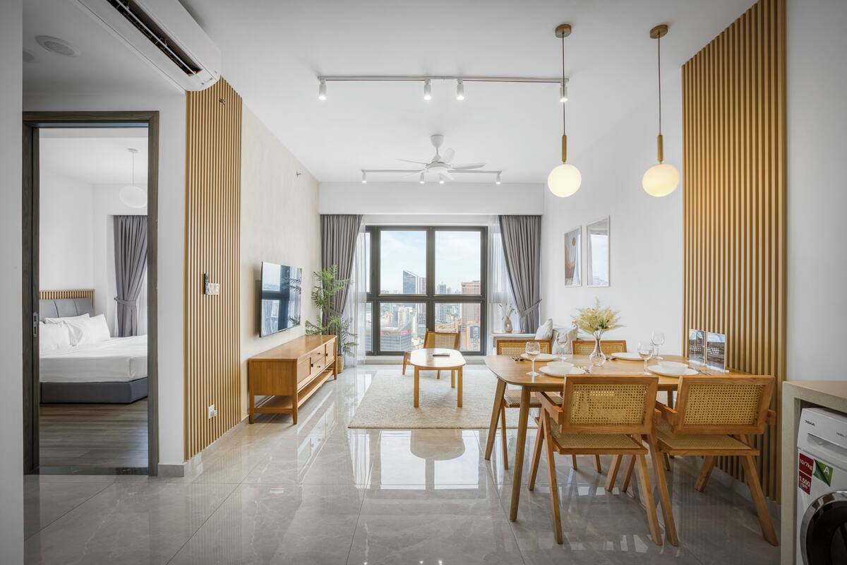 A modern living room with a dining area, a TV, and a large window with a city view.