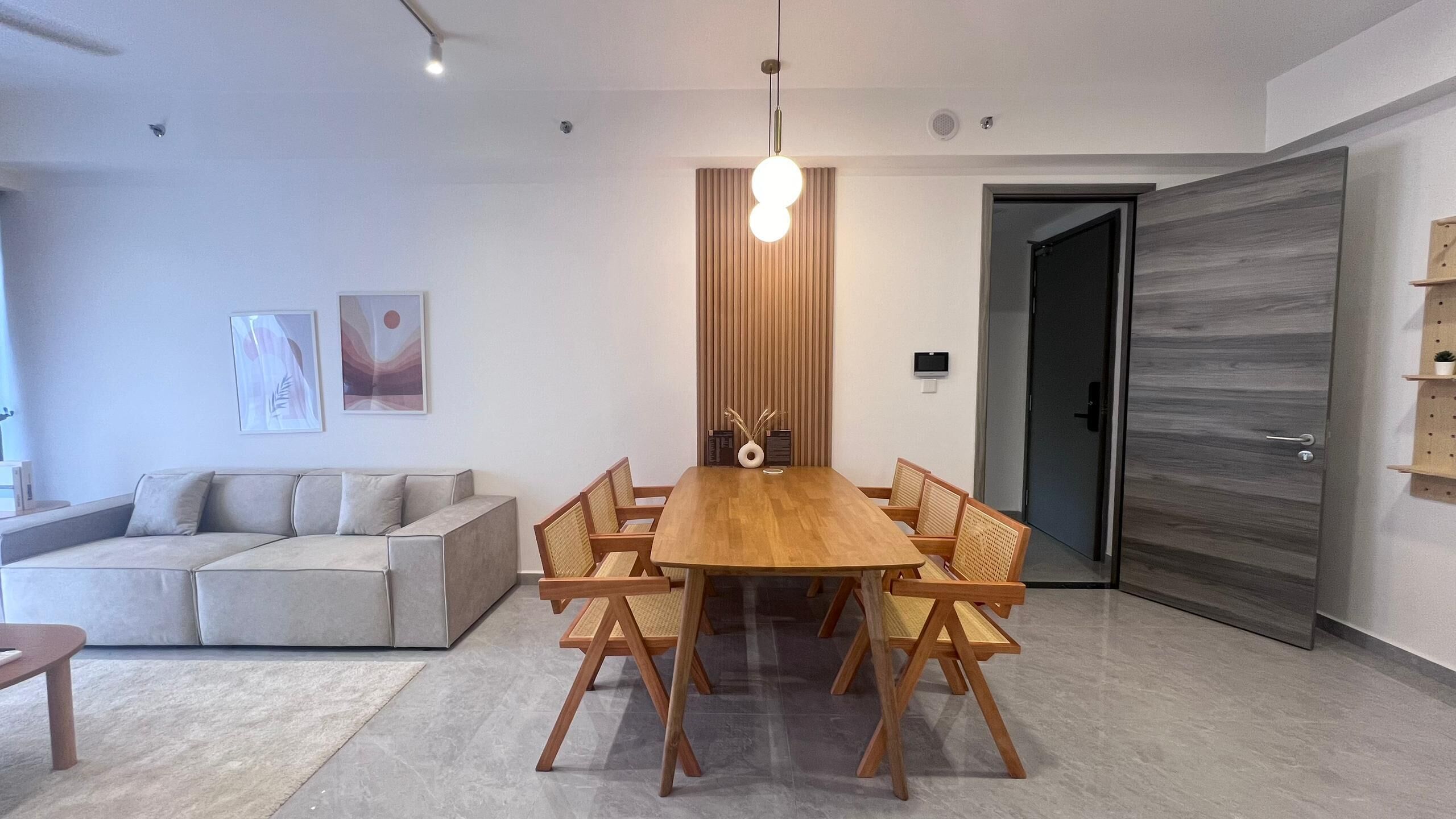 A modern living room with a wooden dining table, a grey sofa, and a wooden floor.