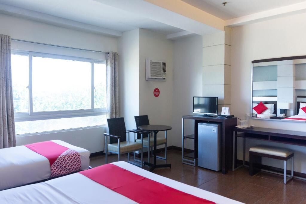 A hotel room with two beds, a desk, a television, and a window with curtains.