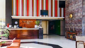 A hotel reception area with a wooden reception desk, a clock, and a television above it. There are two sofas and a small table with decorative items. - EAST VIEW HOTEL (Bacolod)
