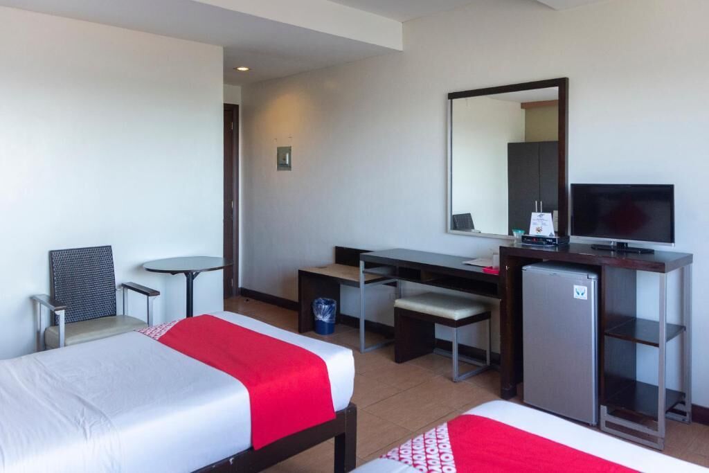 Habitación de hotel con dos camas, un escritorio, una silla, un televisor y un refrigerador.
