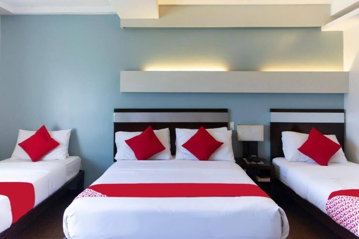 A hotel room with two single beds and a larger bed, all with white bedding and red accents.