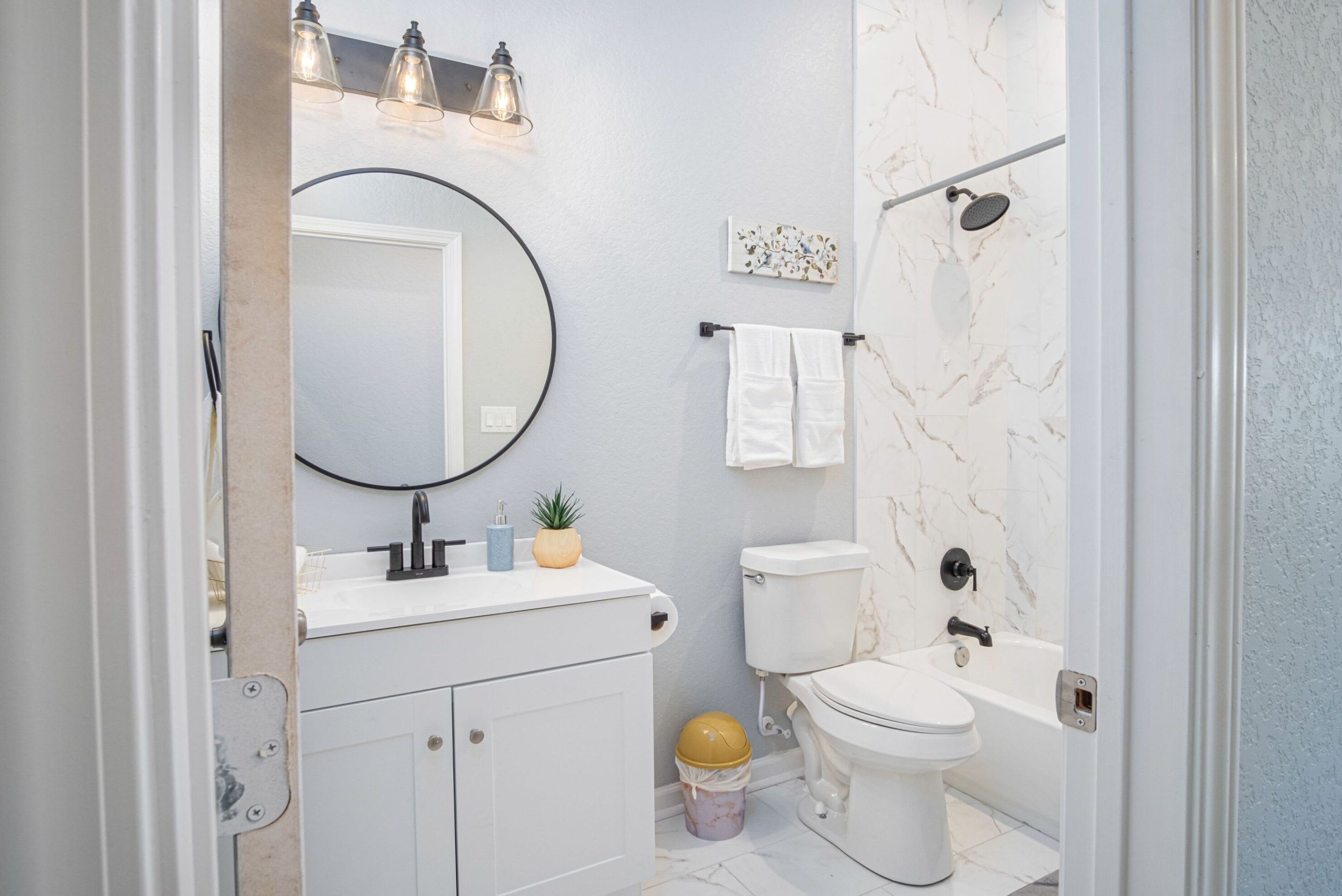 A bathroom with a toilet, sink, and bathtub. There is a mirror above the sink and a light fixture above it.