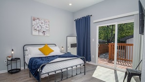 Un dormitorio con cama, mesita de noche, espejo y vistas a una terraza exterior.