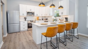 Una cocina moderna con armarios blancos, electrodomésticos de acero inoxidable y una isla central con taburetes de bar.