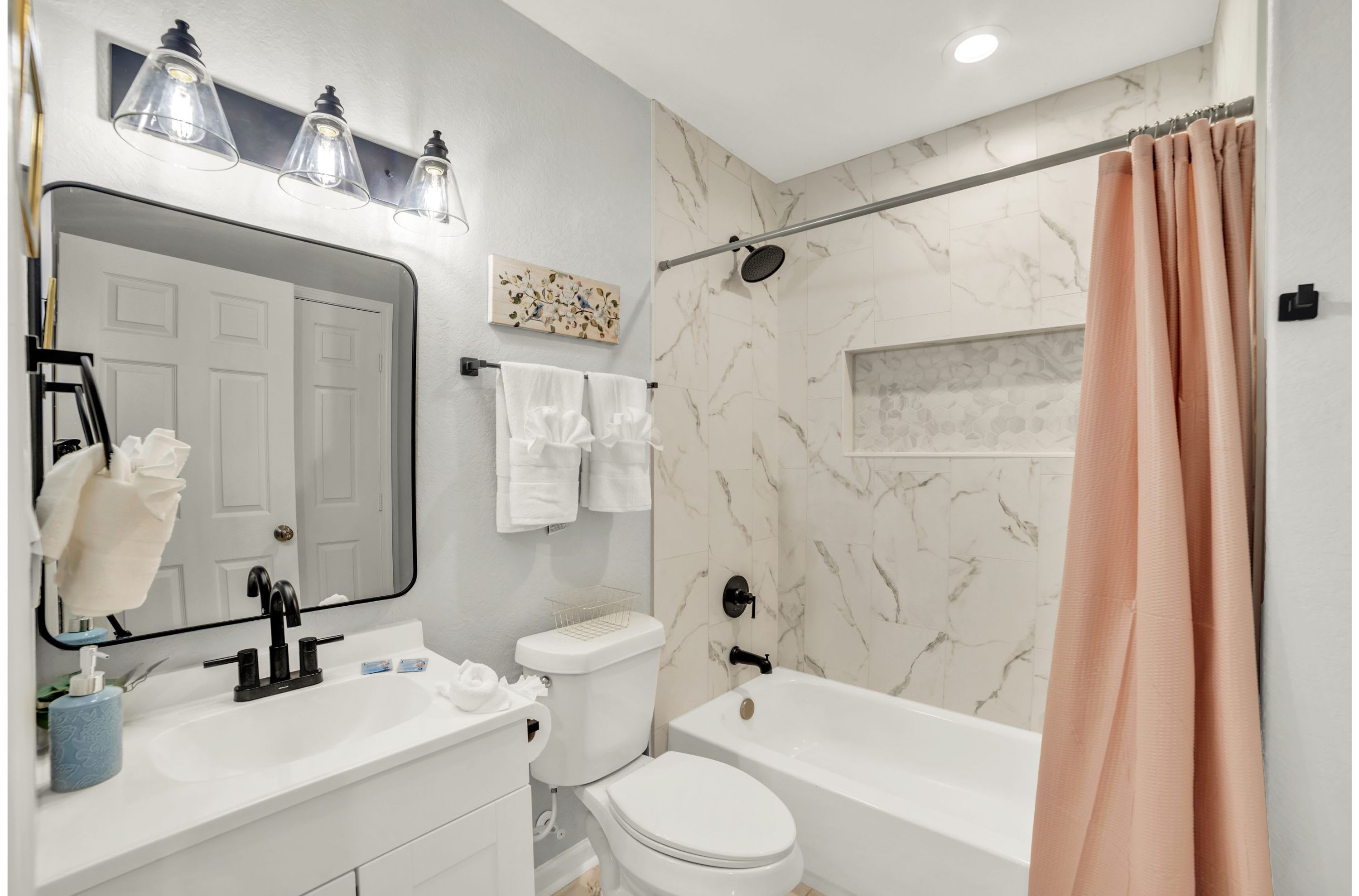 A bathroom with a white sink, mirror, and toilet, a shower with a beige curtain, and marble walls.