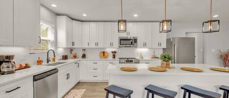 A modern kitchen with white cabinets, stainless steel appliances, and a central island with stools.