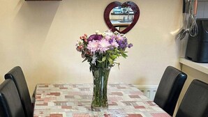 Une table à manger recouverte d’une nappe à motifs, un vase de fleurs et un miroir en forme de cœur accroché au mur.