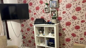 Un salon doté d’un téléviseur à écran plat fixé au mur, d’une étagère blanche ornée de divers objets décoratifs et d’un tapis au motif Union Jack sur le sol.