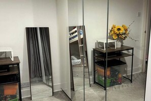 Ein Zimmer mit einem raumhohen Spiegel, einem kleinen Tisch mit einer Blumenvase und einem Bett mit weißem Kopfteil.