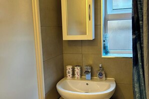 Ein Badezimmer mit Waschbecken, Toilettenpapier, Handseife und einem Fenster.
