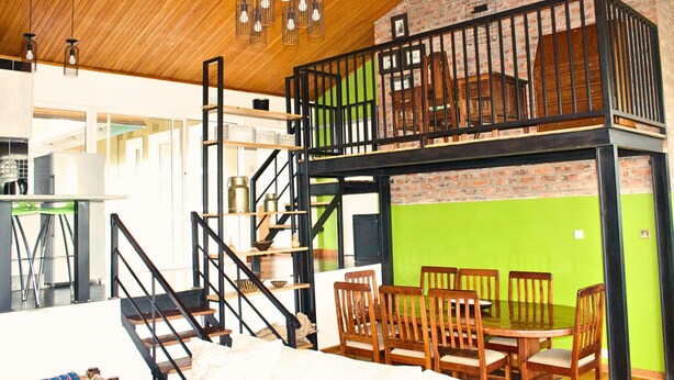 Un espace repas avec une table haute et des chaises, un escalier avec une rampe, et une mezzanine avec une rampe et vue sur l’intérieur.