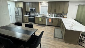A modern kitchen with a dining area, featuring a central island, built-in appliances, and a herringbone-patterned backsplash. - Amazing Home Away From Home (Valdosta)