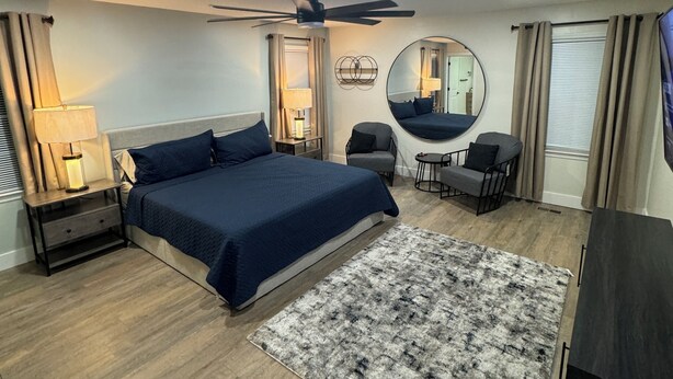 A modern bedroom with a large bed, a ceiling fan, a round mirror, and a small desk with a chair. - Amazing Home Away From Home (Valdosta)