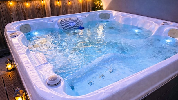 A hot tub with a wooden deck and string lights, surrounded by a wooden fence.