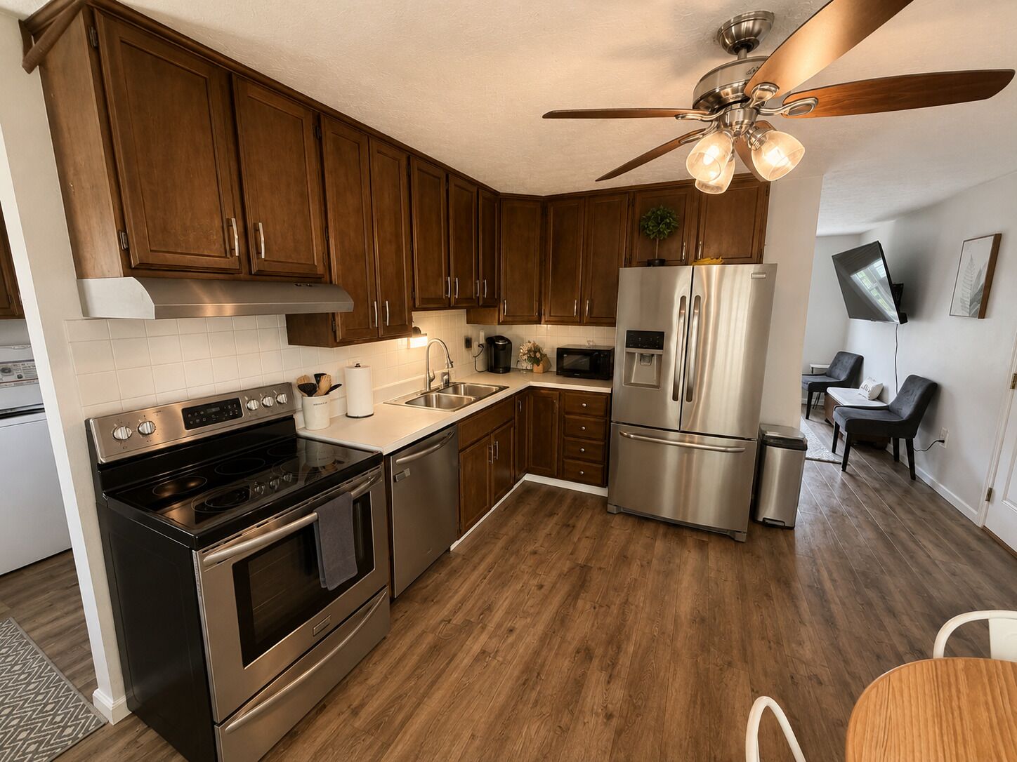 Et moderne køkken med træskabe, rustfrie stålapparater, en loftsvifte og et spiseområde med et bord og stole.