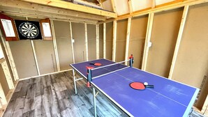 A room with two ping pong tables, a dartboard, and wooden paneling.