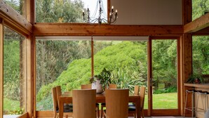 Ein Essbereich mit Holztisch und Stühlen, einer Kronleuchter und Blick auf einen üppigen Garten durch große Fenster.