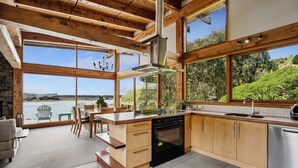 Eine moderne Küche mit großen Fenstern, Holzbalken und Blick ins Freie.