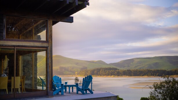 Ein modernes Haus mit Glastür und einer Terrasse mit Blick auf einen See, inklusive Stühlen.