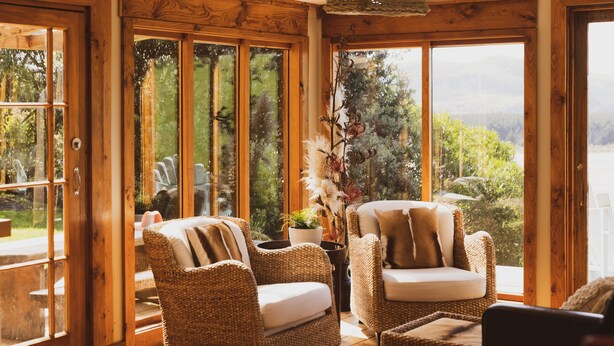 Un cuarto acogedor con sillas de mimbre, un sofá y un amplio ventanal con vistas a la vegetación y montañas.