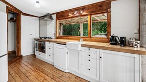 Una cocina con suelo de madera, armarios blancos, horno empotrado y ventana con marco de madera.