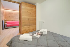 Un dormitorio con una cama acolchada gris, un armario de madera, una colcha roja y un radiador blanco.