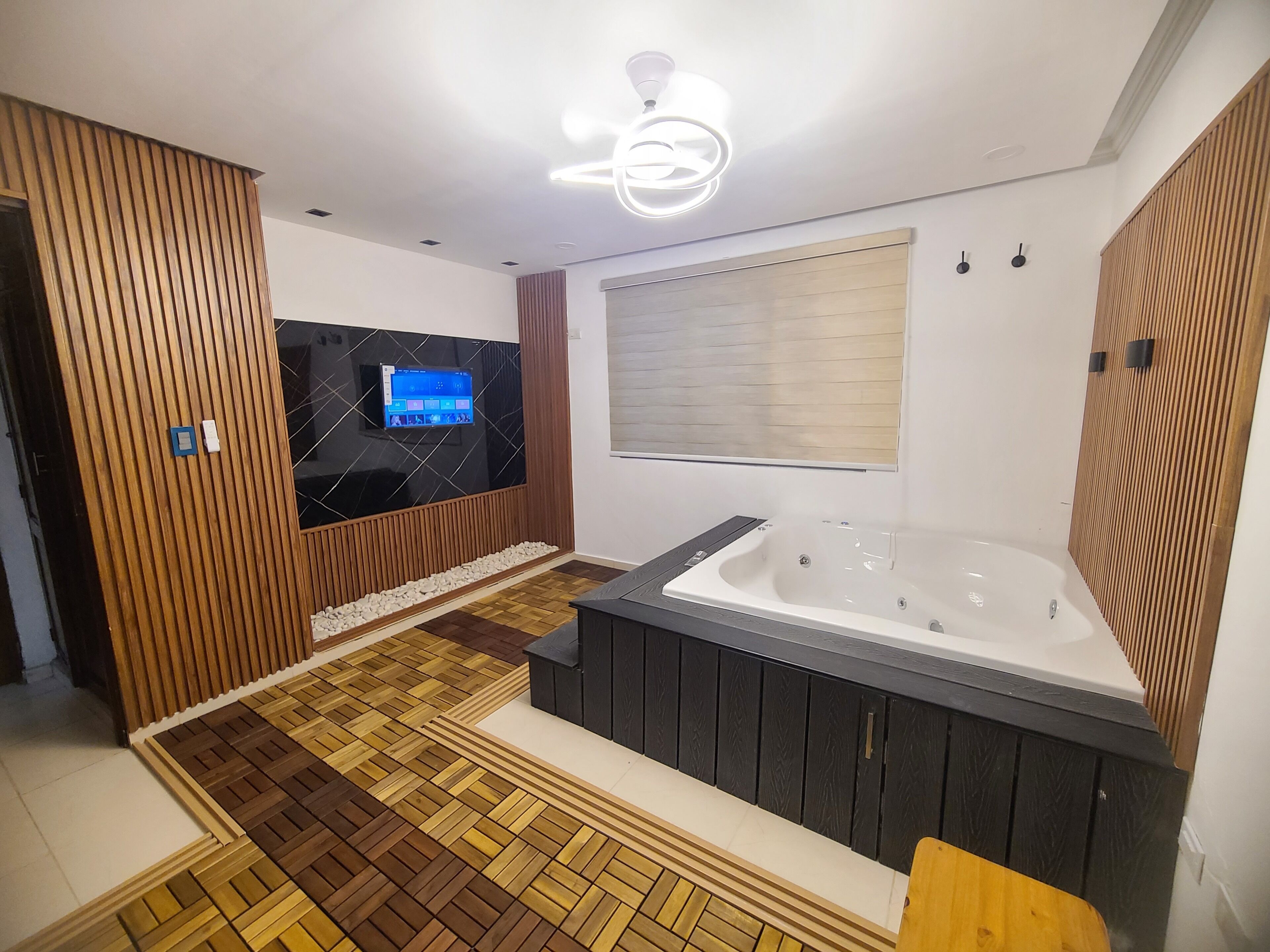 A modern bathroom with a wooden floor, a bathtub, a vanity, and a wall-mounted TV.