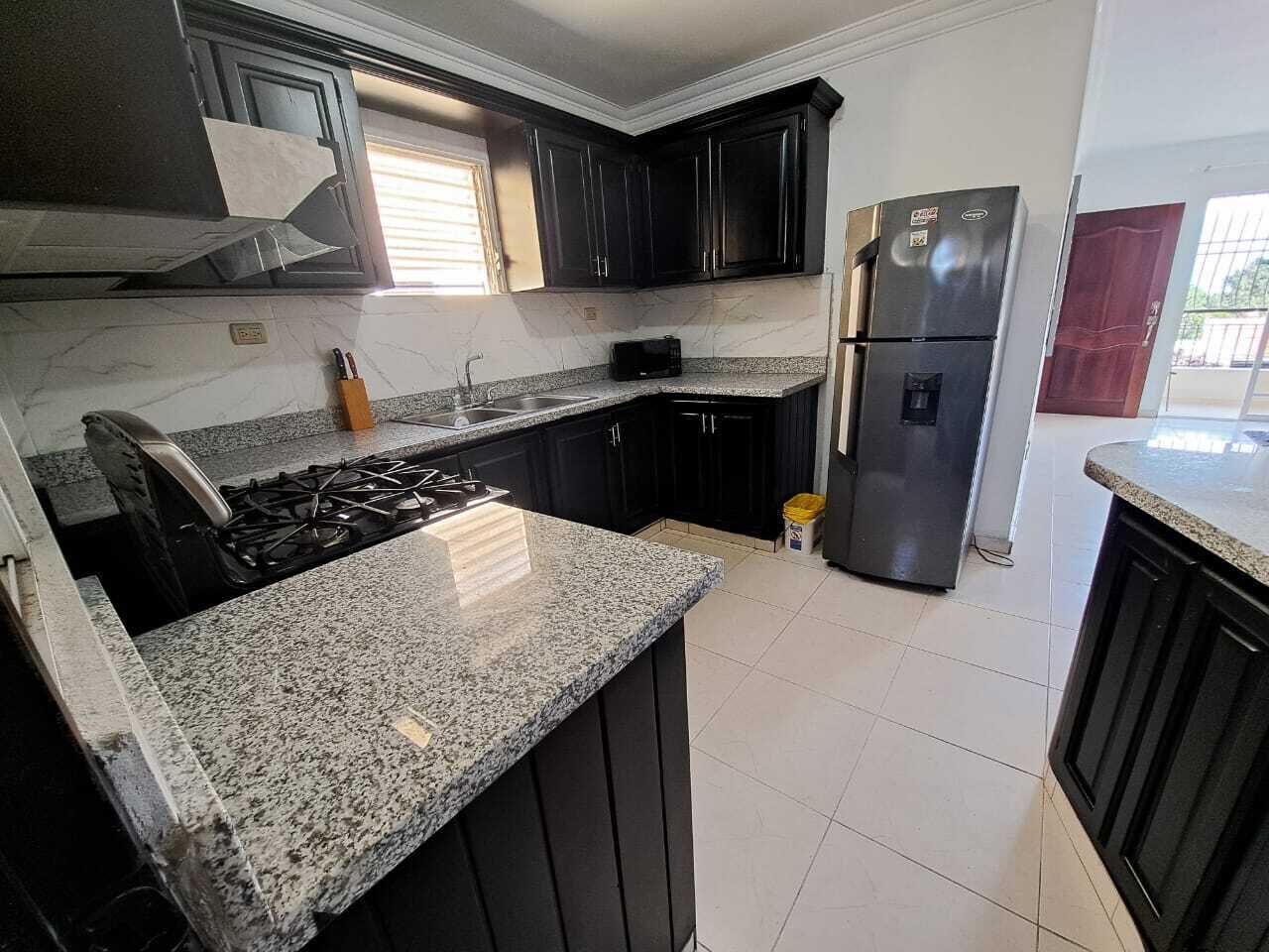 Uma cozinha com armários escuros, bancada de granito, fogão de aço inoxidável e geladeira.