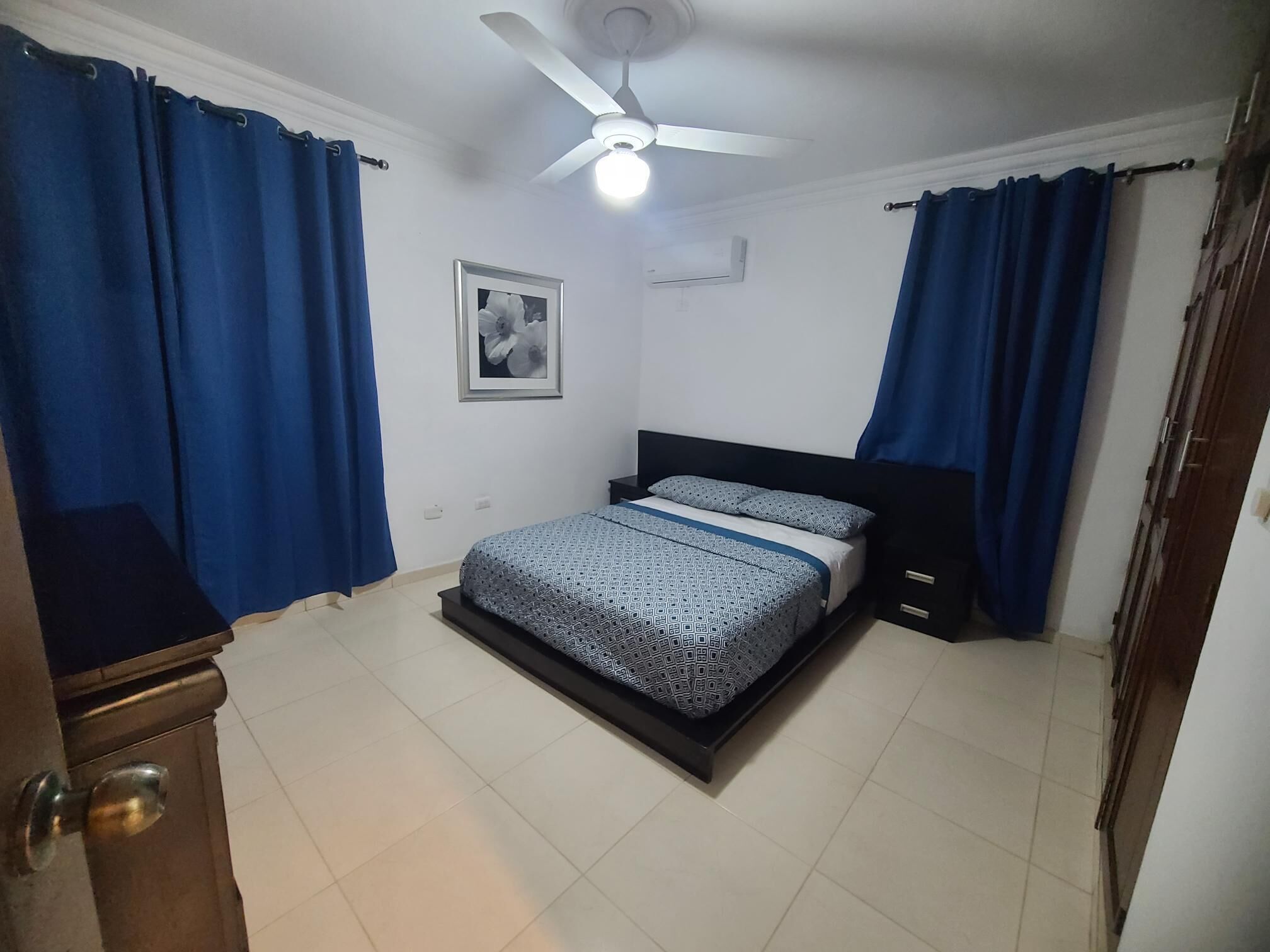 A bedroom with a bed, curtains, a ceiling fan, and a framed picture on the wall.