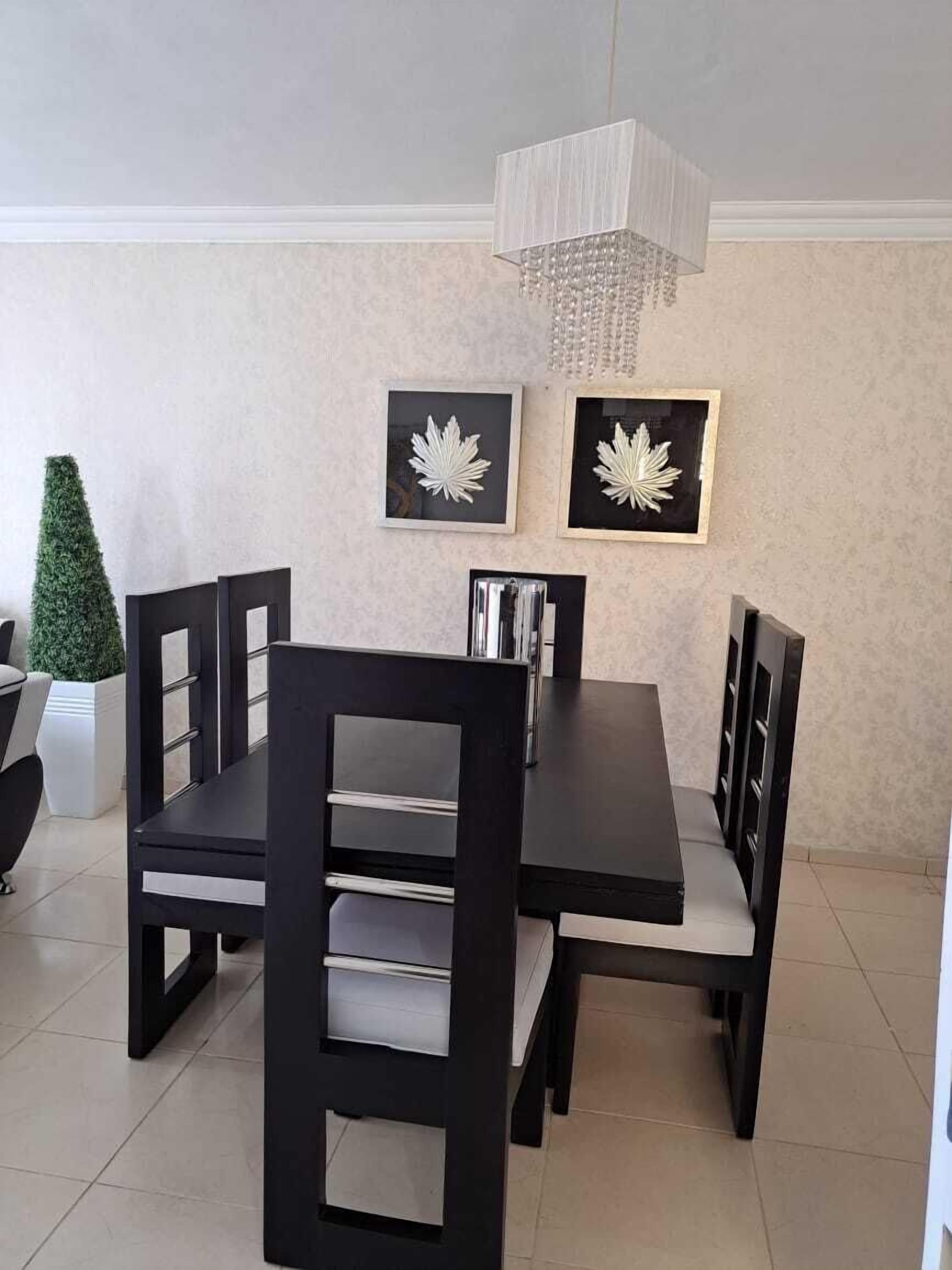 Un comedor con una mesa rectangular, seis sillas y dos adornos con forma de hojas enmarcados en la pared.