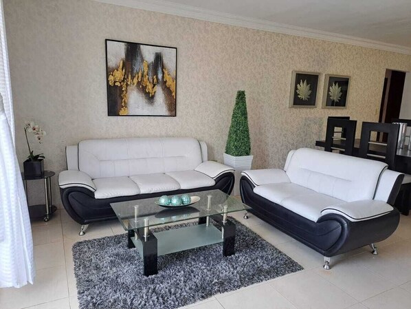 A modern living room with two white sofas, a glass coffee table, and a decorative plant. - Céntrico con Jacuzzi privado (Santiago de los Caballeros)