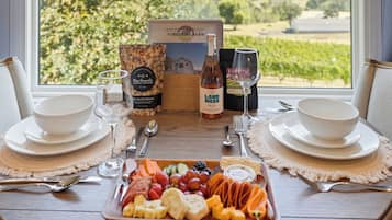 A dining table set with white plates, bowls, cutlery, and a fruit platter, with a bottle of wine and a glass of wine in the background.