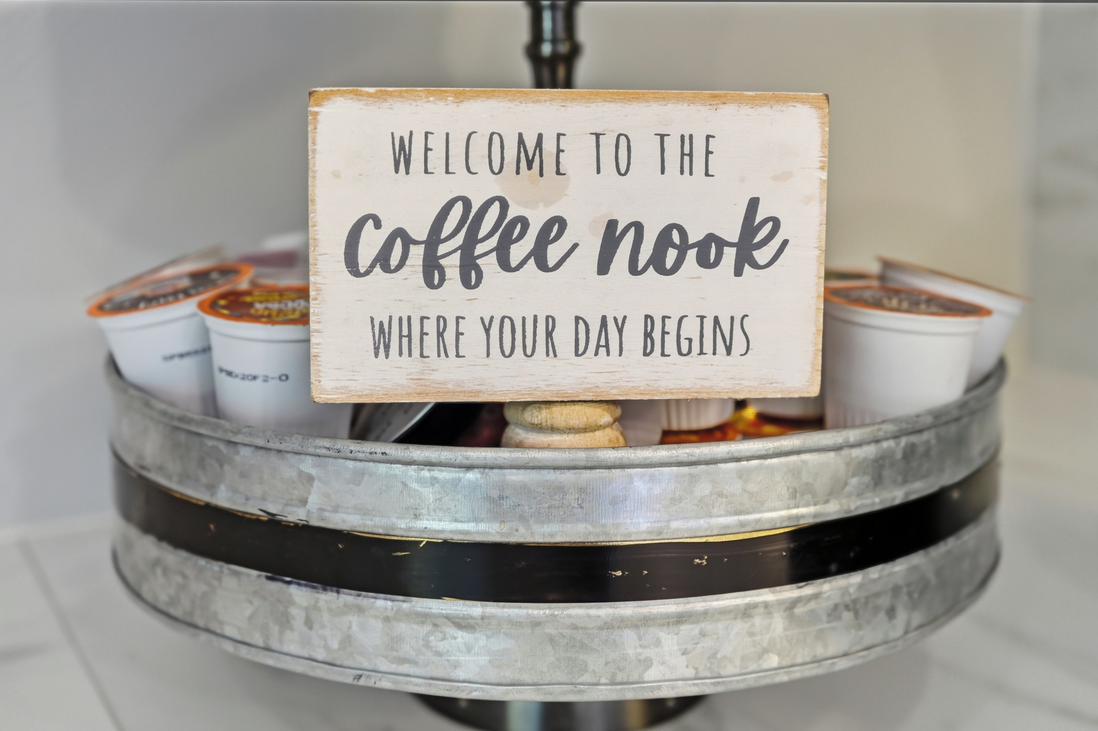 Un cartel con el texto 'BIENVENIDOS A LA ESQUINA DEL CAFÉ, DONDE COMIENZA TU DÍA' colocado sobre una cafetera.
