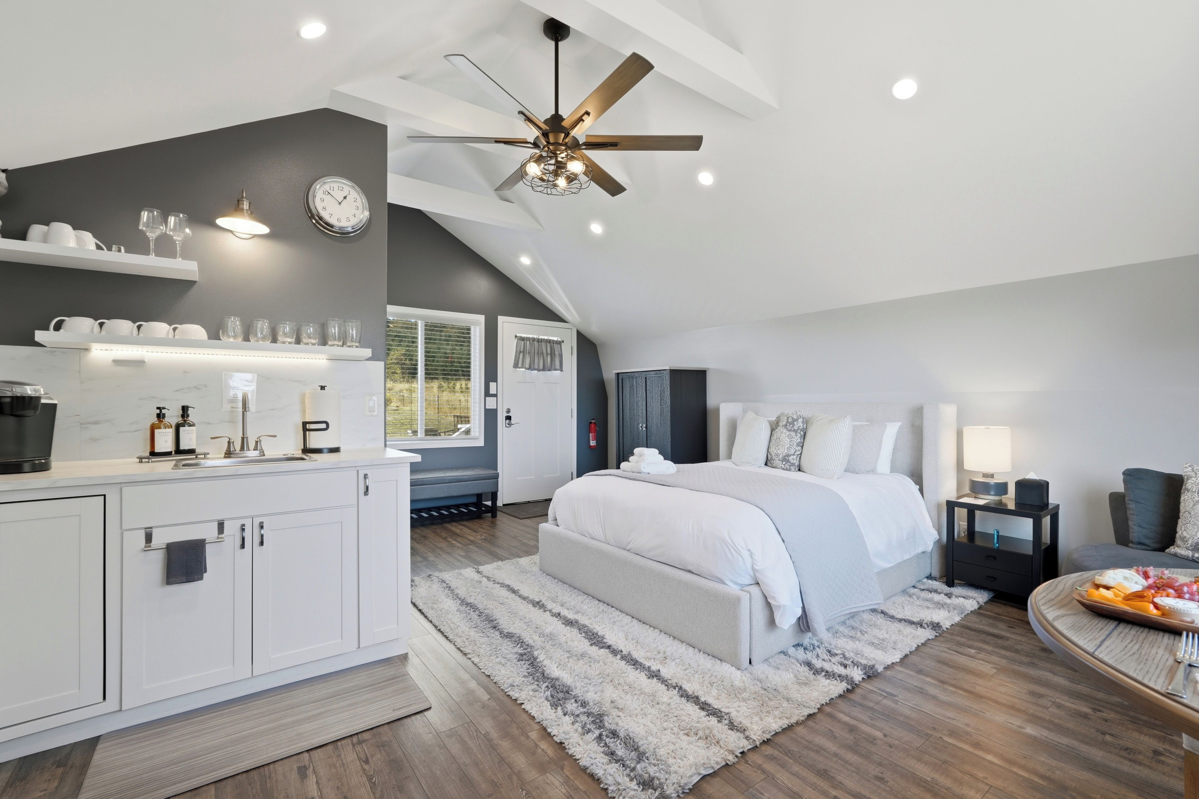 A modern bedroom with a large bed, a ceiling fan, and a view of the outdoors.
