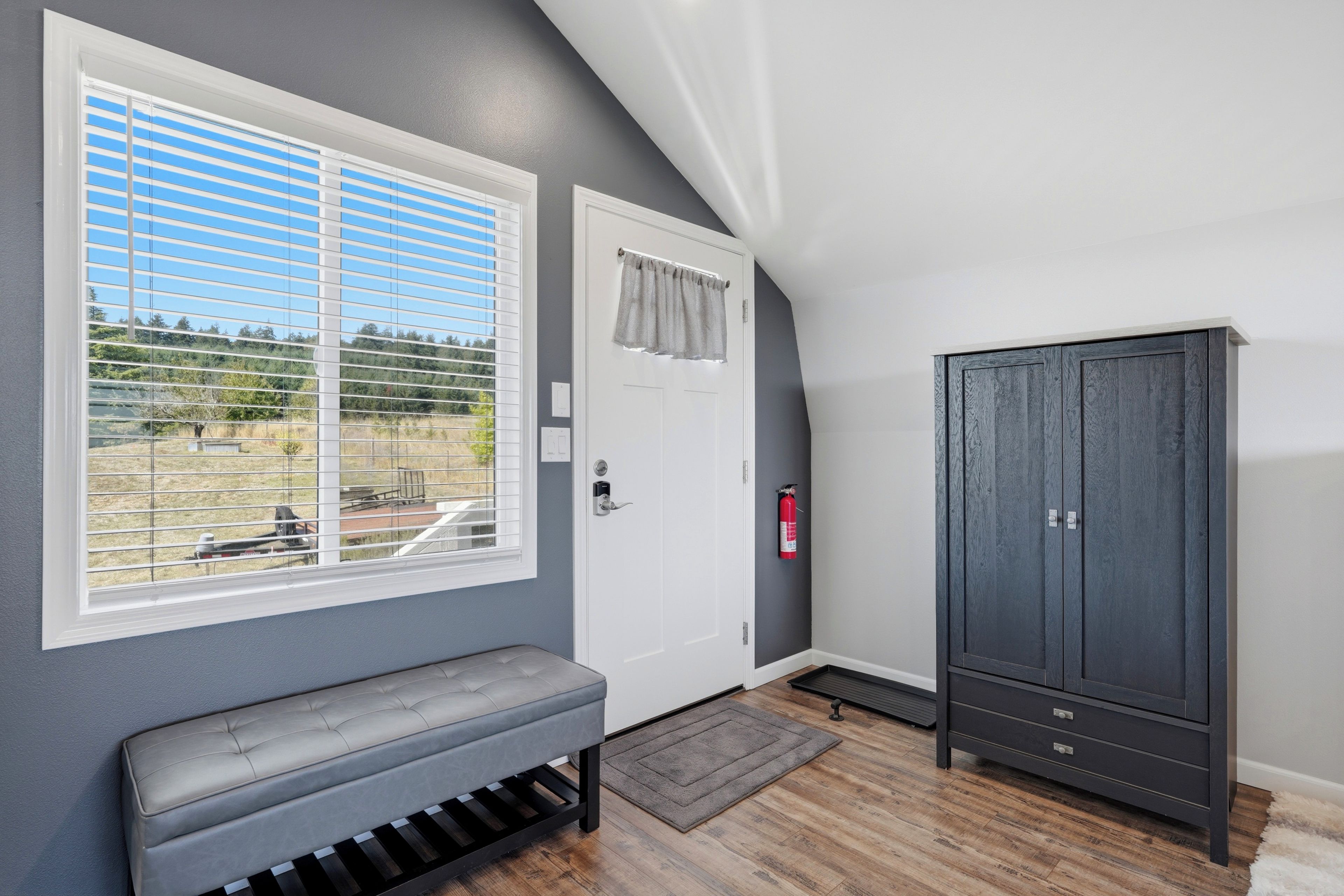 Ein Zimmer mit einer Bank, einer Tür, einem Kleiderschrank und einem Fenster mit Jalousien.
