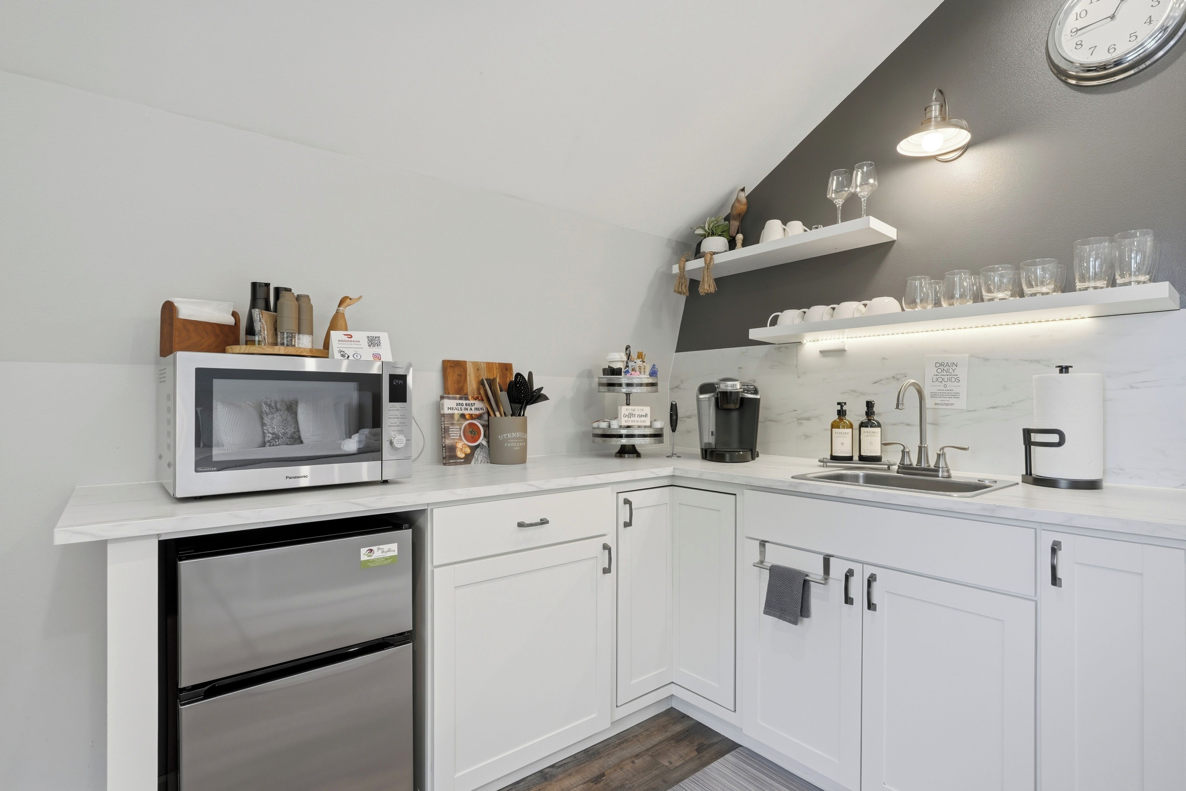 A modern kitchen with white cabinetry, a built-in microwave, a coffee maker, and a sink.
