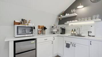 A modern kitchen with white cabinetry, a built-in microwave, a coffee maker, and a sink.