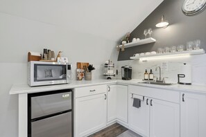 Une cuisine moderne avec des meubles blancs, un four à micro-ondes encastré, une machine à café et un évier.