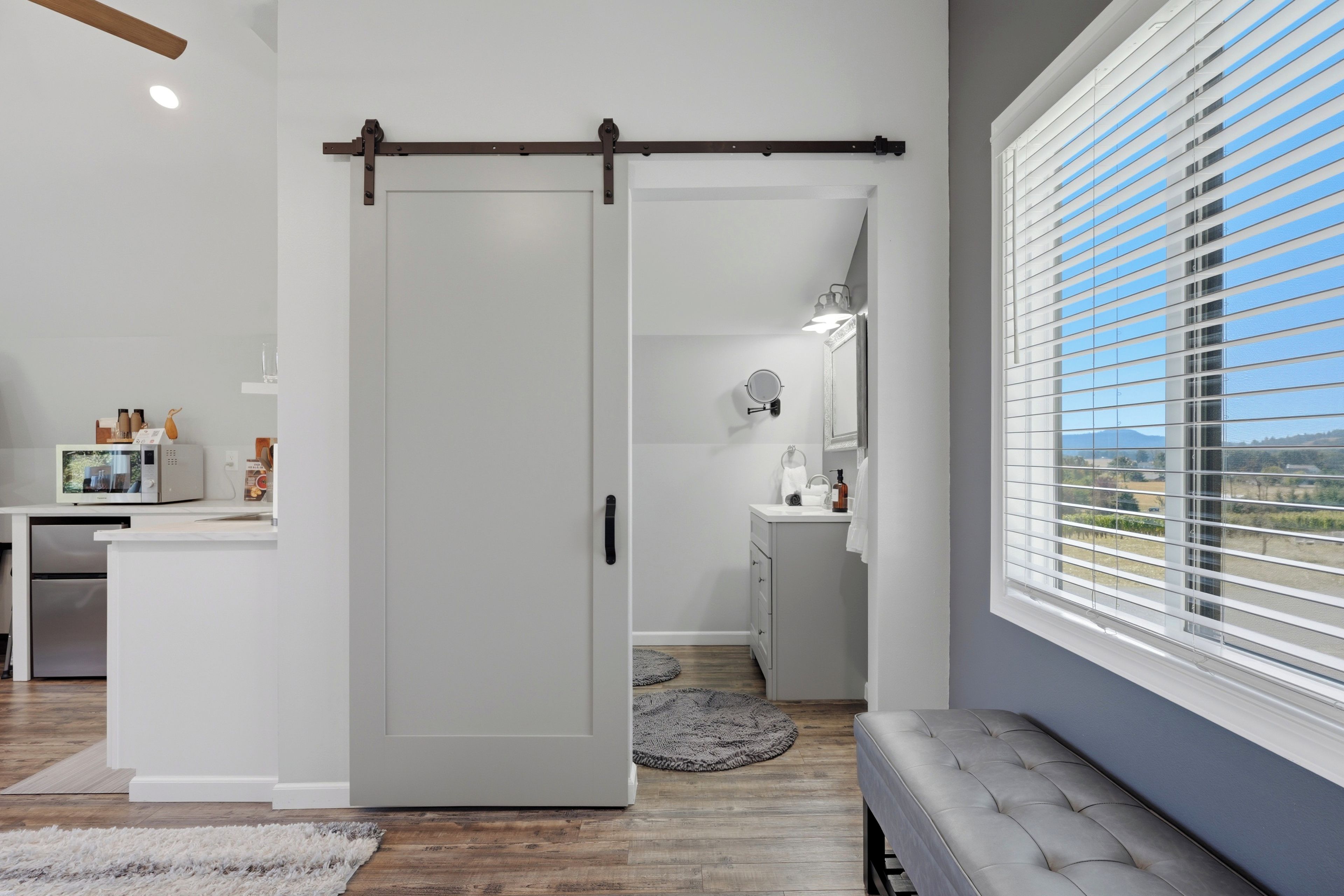 Een modern interieur met een schuifdeur naar een badkamer, een keuken met een magnetron, en een groot raam met zonwering.
