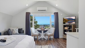 Ein Schlafzimmer mit Bett, Esstisch mit Stühlen, Fernseher und Blick ins Freie.